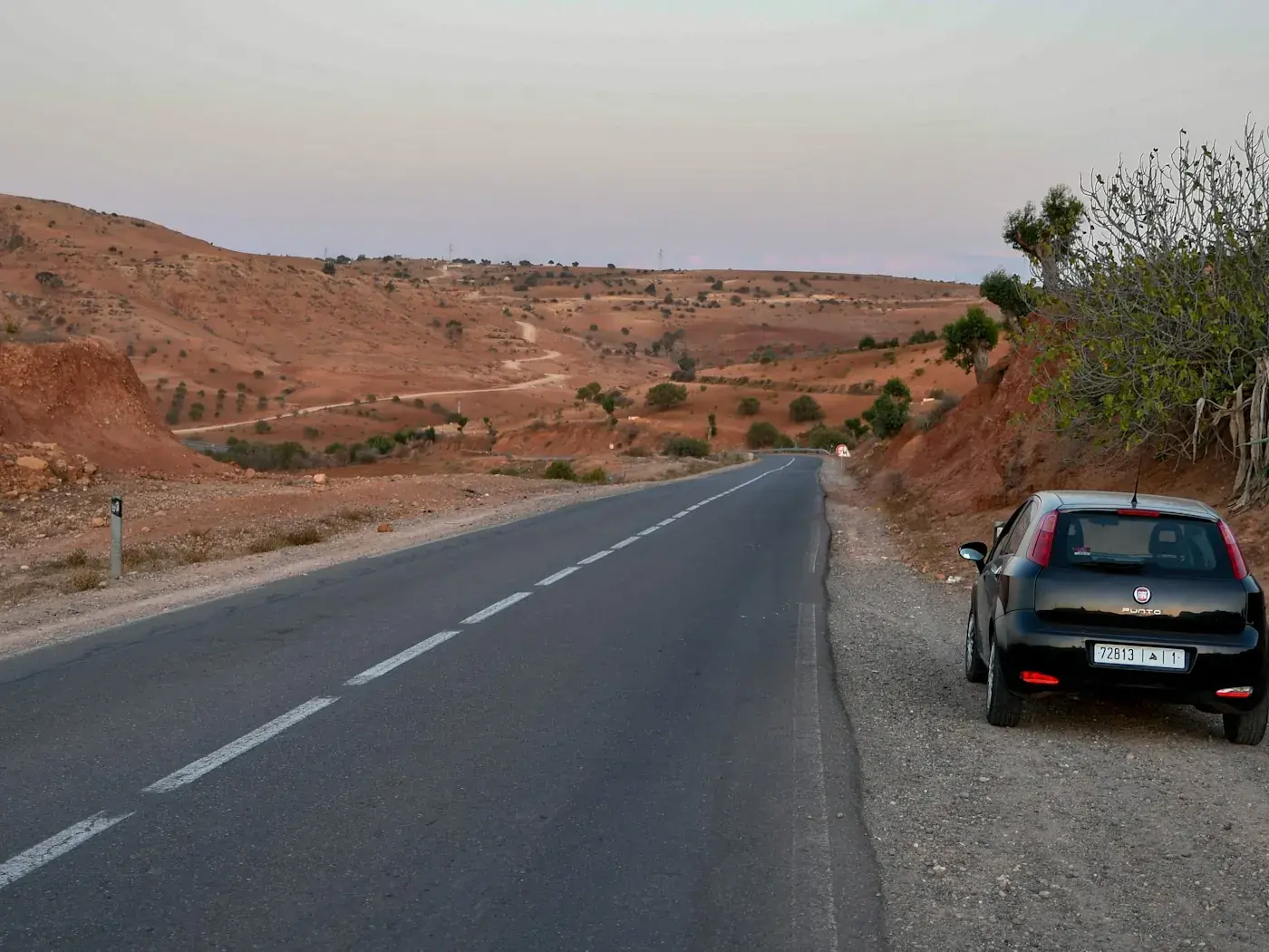 A narrow asphalt road crossing the Moroccan desert under a clear sky.