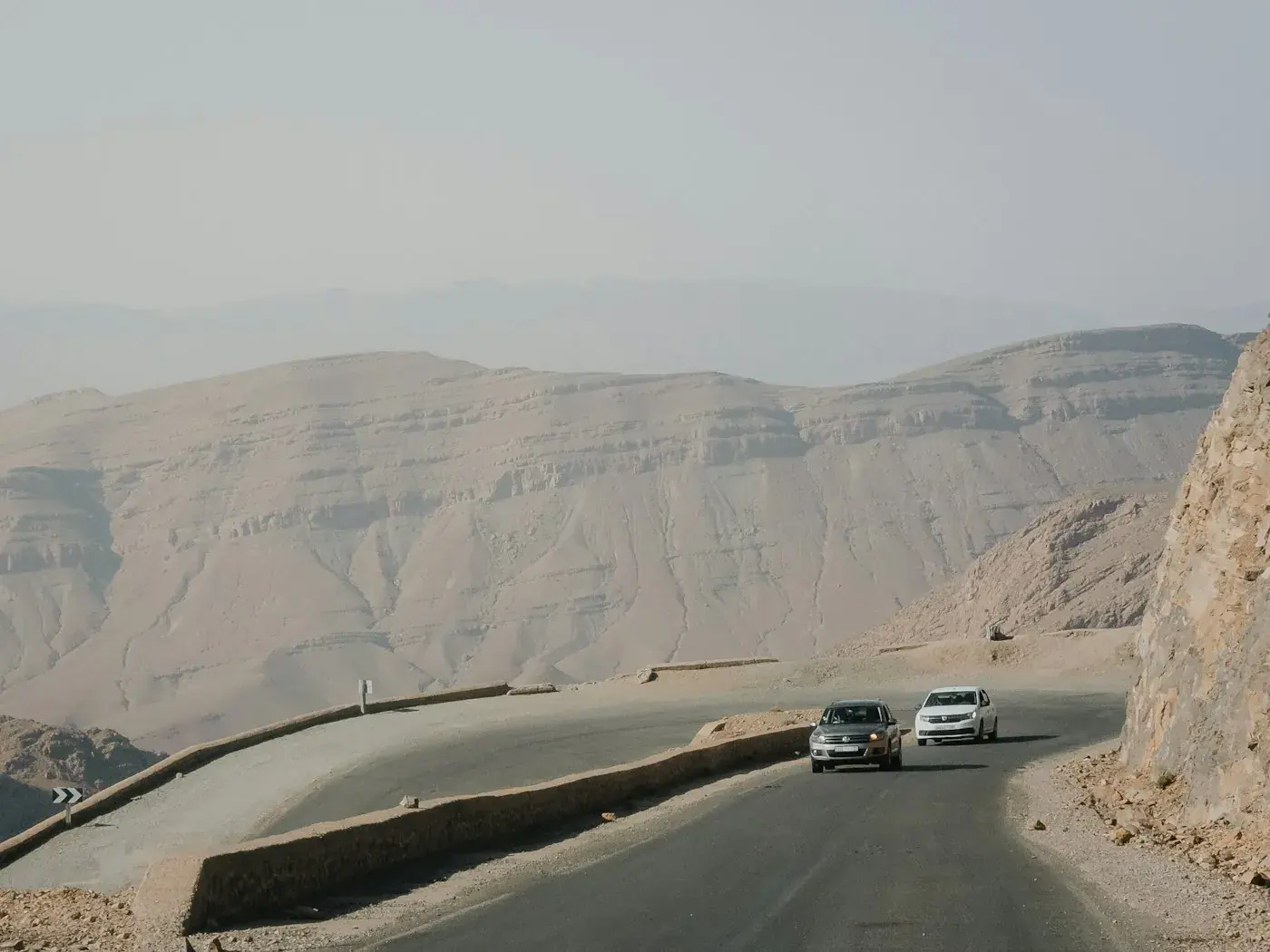 Two vehicles on a winding road through the desert mountains.