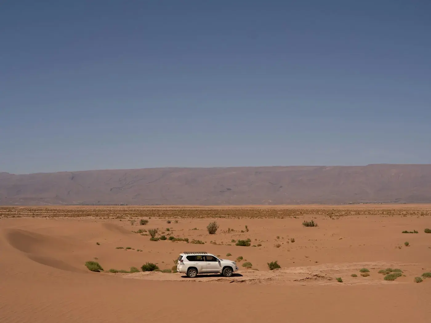 A white 4x4 driving along a sandy desert track.